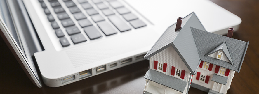 A miniature house model is beside a laptop computer